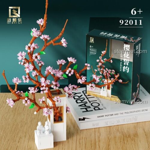 Đồ chơi mô hình Cây hoa anh đào Qizhile 92011 đặt cạnh sách, thể hiện kích thước tương đối, món quà đáng tiền cho bé gái.