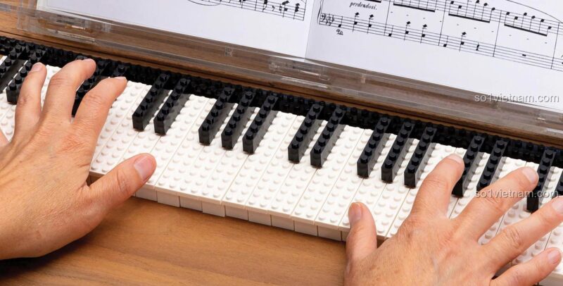 Sách nghệ thuật LEGO của Chronicle ISBN9781452179629, hình ảnh đôi tay đang chơi đàn piano làm từ gạch LEGO® trắng và đen, thể hiện sự sáng tạo bất tận.