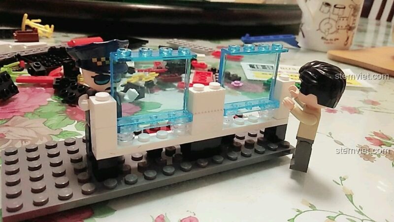 Cảnh các nhân vật học sinh và giáo viên đang chờ tại trạm xe buýt đã lắp xong từ bộ đồ chơi QMAN 1136 giá tốt.