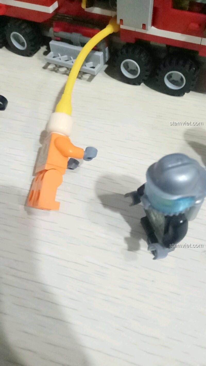 Minifigure lính cứu hỏa đang sử dụng vòi nước trong bộ đồ chơi SEMBO 603034, thể hiện tính năng phun nước thực tế