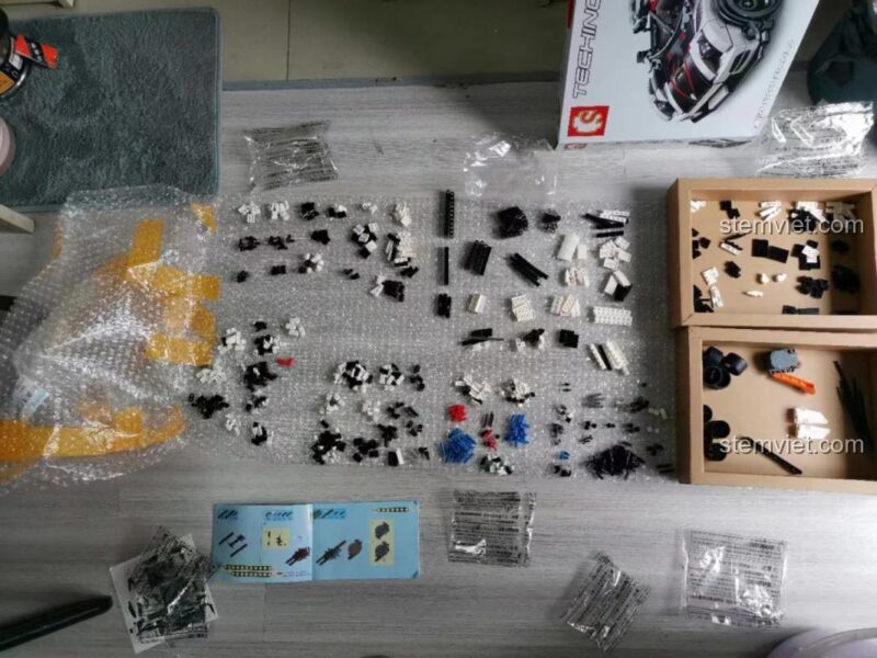 Toàn bộ các chi tiết, sách hướng dẫn và hộp của bộ đồ chơi Xe đua Koenigsegg SEMBO 701707 được bày ra chuẩn bị lắp ráp. Sản phẩm phù hợp cho bé trai từ 6 tuổi.