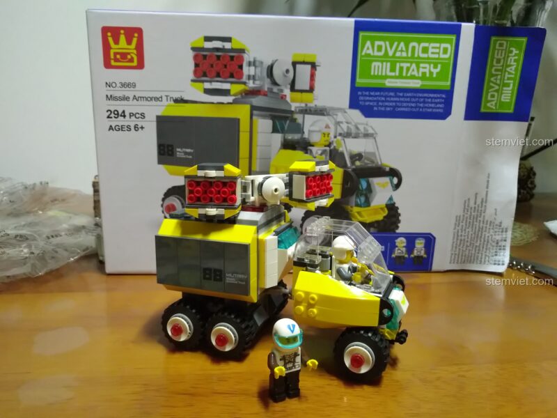 Mô hình WANGE 3669 Xe Bọc Thép Phóng Tên Lửa đã hoàn thiện cùng 2 minifigure phi công, đặt cạnh hộp sản phẩm.