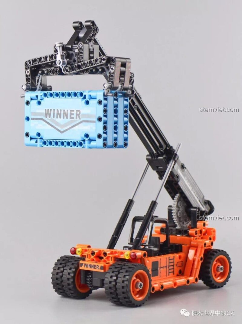 Mô hình Xe Nâng Gắp Container Winner 7059 đang thực hiện thao tác gắp và nâng container một cách vững chãi.