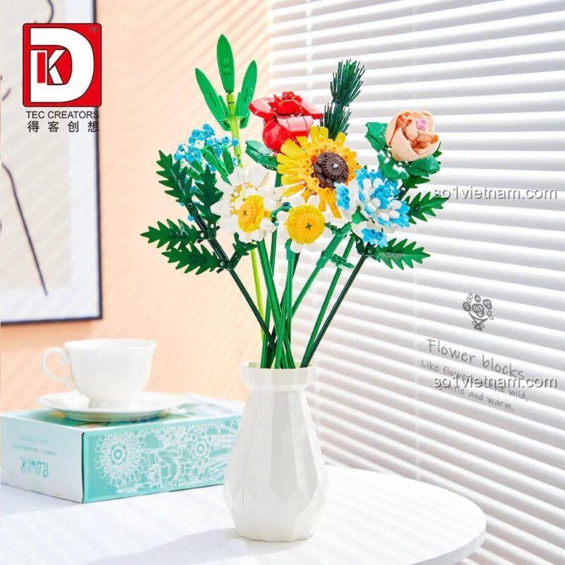 Bó hoa lắp ghép DK 3027 trong lọ hoa trắng, bên cạnh ly cà phê và hộp sản phẩm, tạo nên góc trang trí đẹp mắt, đồ chơi giáo dục cho bé gái 8 tuổi