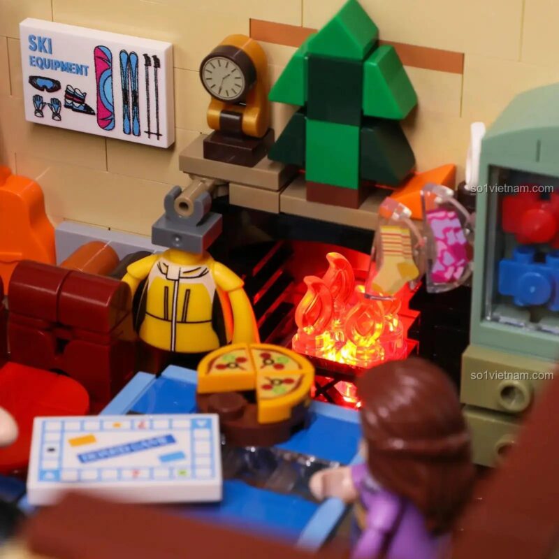 Các minifigures đang tụ tập chơi board game và ăn pizza bên trong đồ chơi mô hình Ngôi Nhà Gỗ Phủ Tuyết.