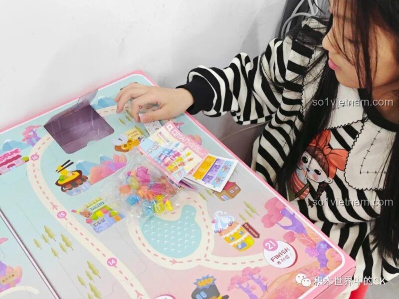 Một bé gái khác đang mở ô quà và xem các mảnh ghép nhiều màu sắc của bộ QMAN 35018.