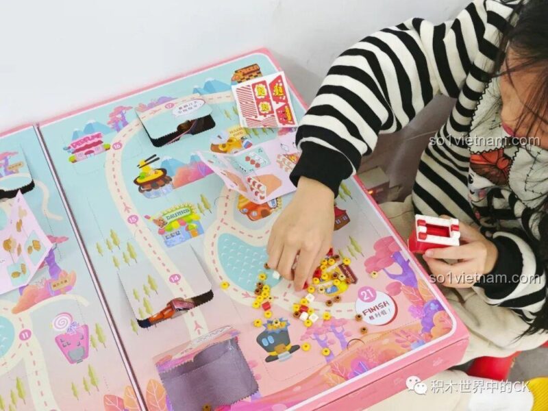 Bé gái lắp ráp mô hình máy ảnh đồ chơi từ một trong các ô quà của bộ QMAN 35018.