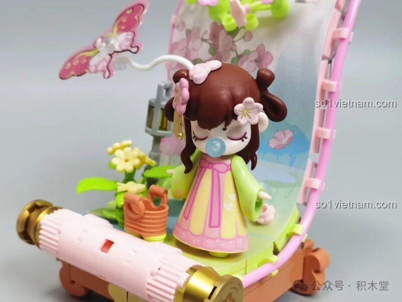 Nanci đứng duyên dáng bên giỏ hoa vàng, một chi tiết đáng yêu của đồ chơi trang trí Mô hình trang trí chủ đề mùa xuân.
