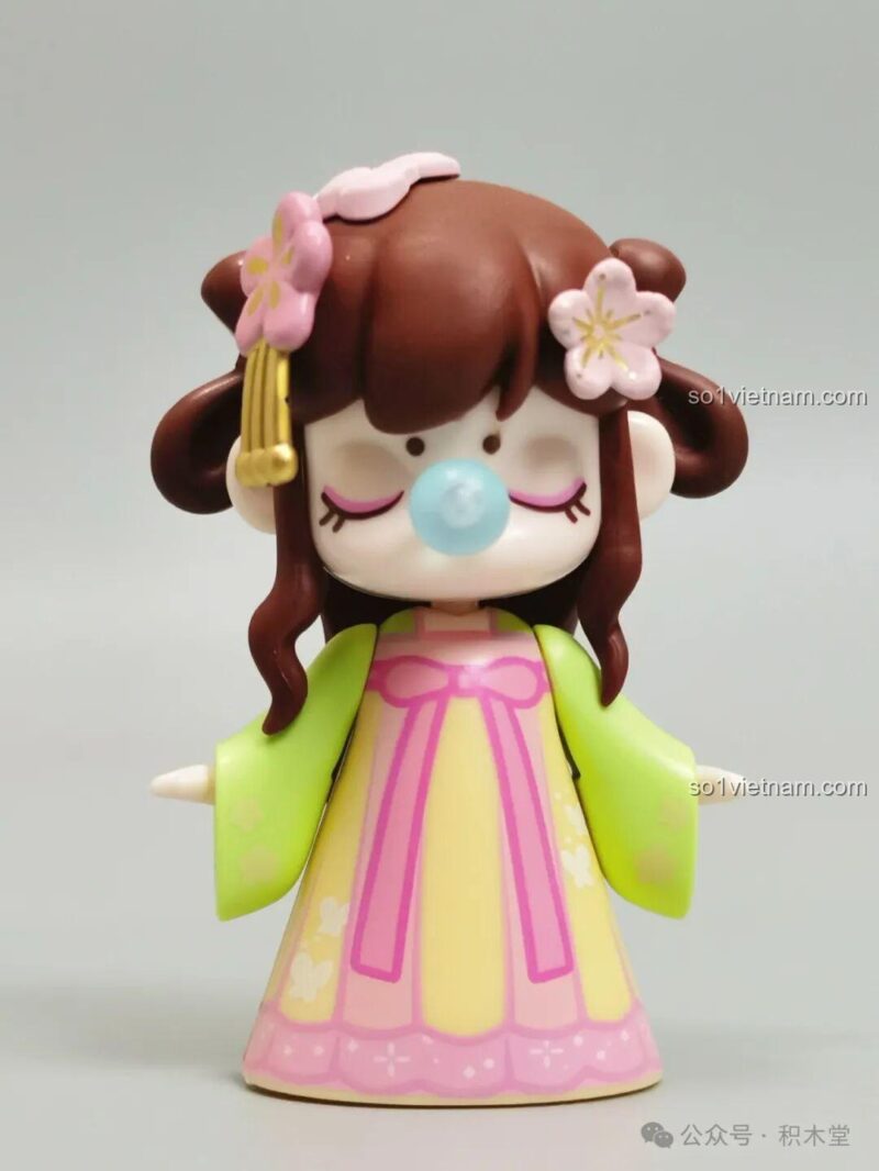 Cận cảnh figure Nanci đi kèm, mặc trang phục cổ trang màu xanh và vàng, có hoa cài tóc.